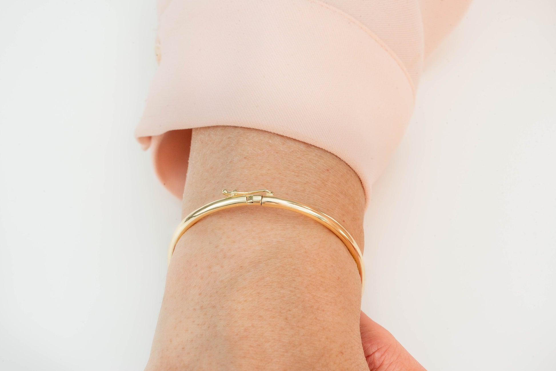 A round bangle bracelet made of 14k gold, displayed on a wrist.