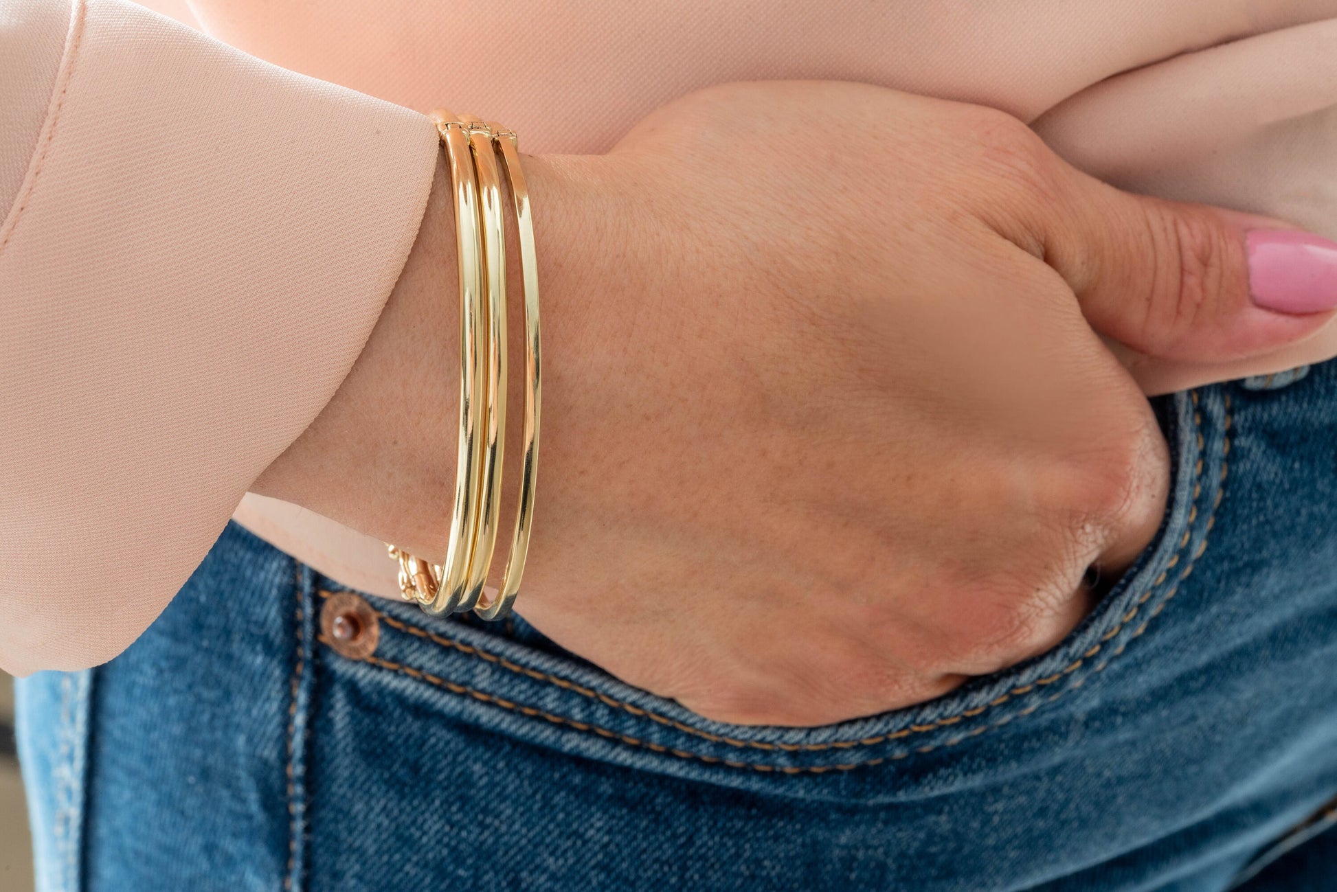 The image depicts a collection of gold bangle bracelets encircling a person's wrist, each crafted from 14k gold.