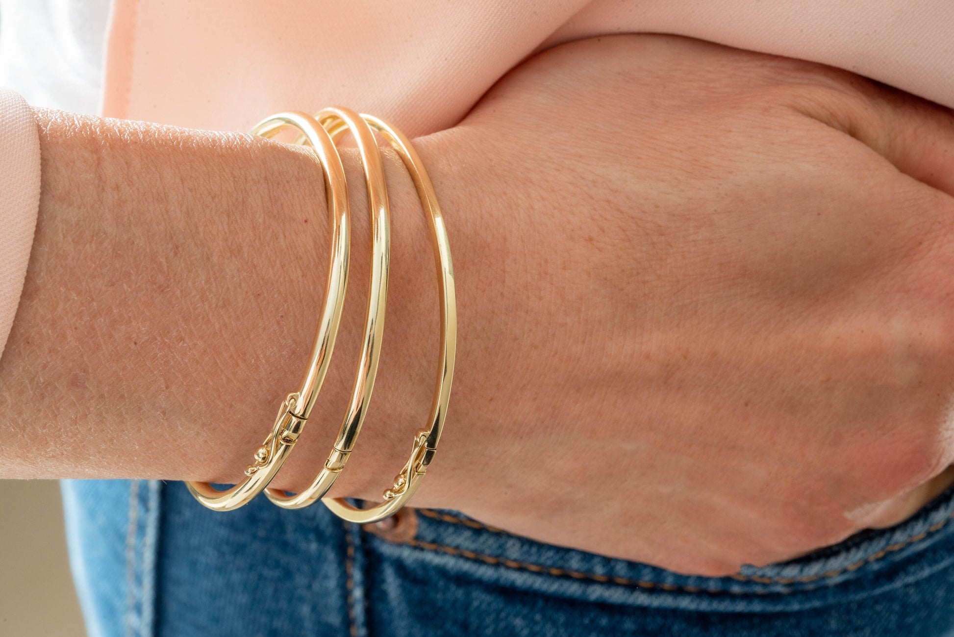 The image depicts a collection of gold bangle bracelets encircling a person's wrist, each crafted from 14k gold.