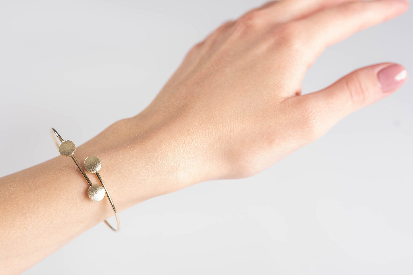 This photo features a minimalist gold open cuff bracelet with three textured round accents on the top.