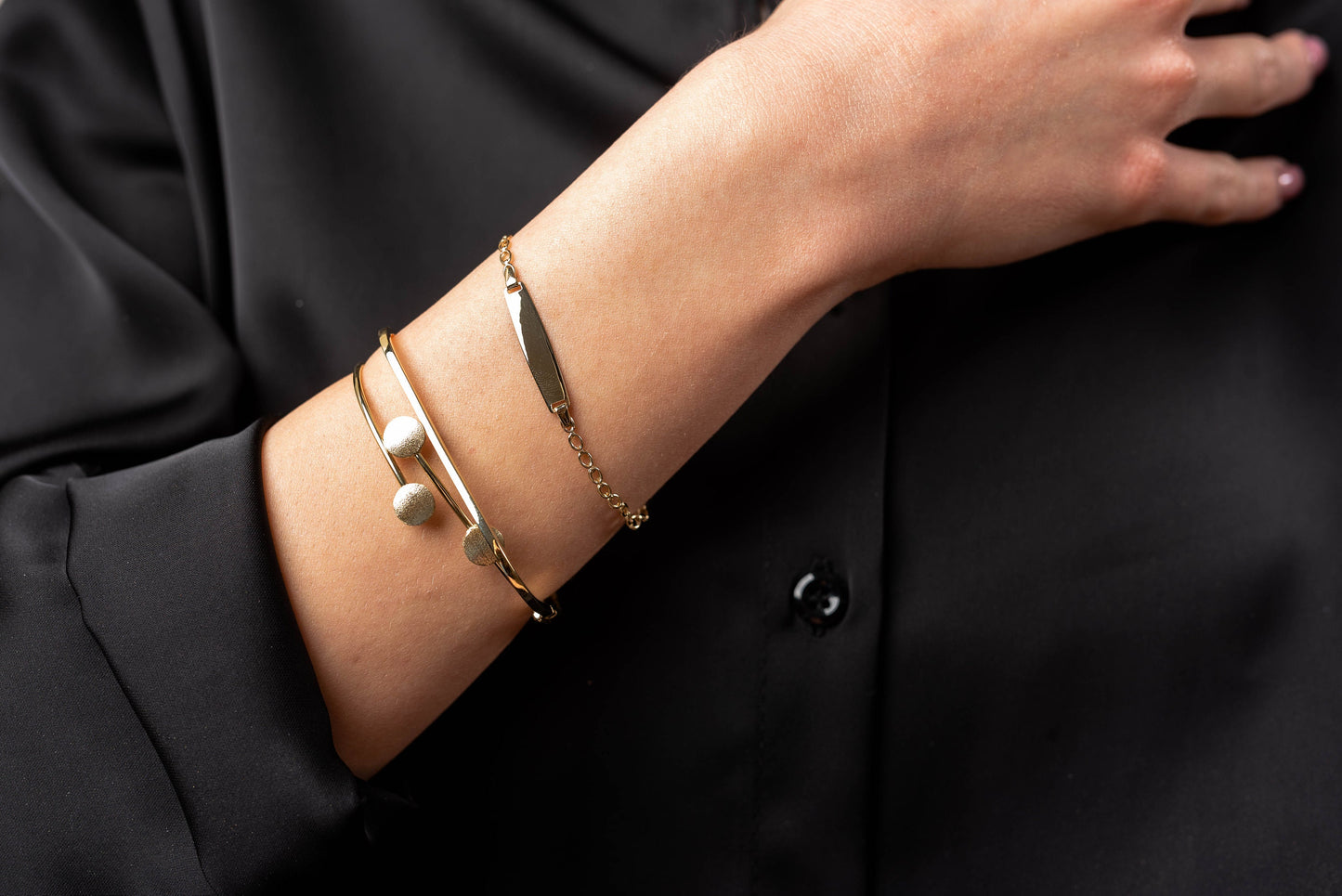 This is an image featuring several gold bracelets on a person's wrist. The bracelets vary in style, including a delicate chain bracelet, a flat bar bracelet, and a couple of minimalist bangle design