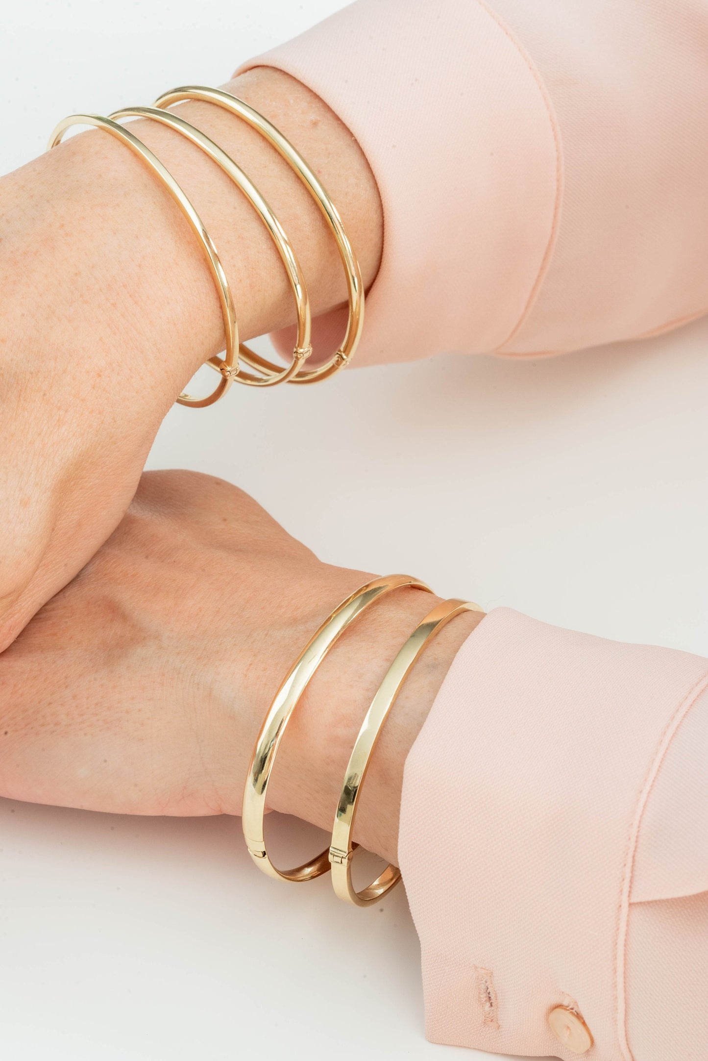 The image shows a close-up of two wrists adorned with several gold bangle bracelets