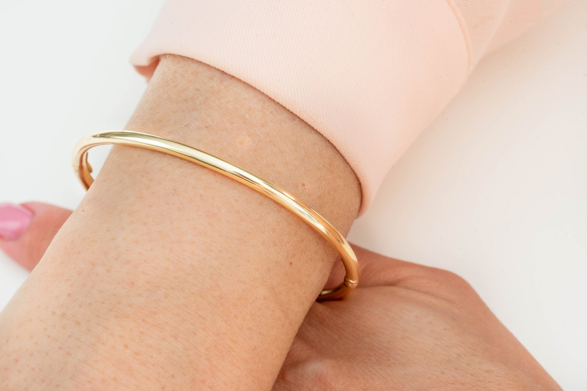 A round bangle bracelet made of 14k gold, displayed on a wrist.