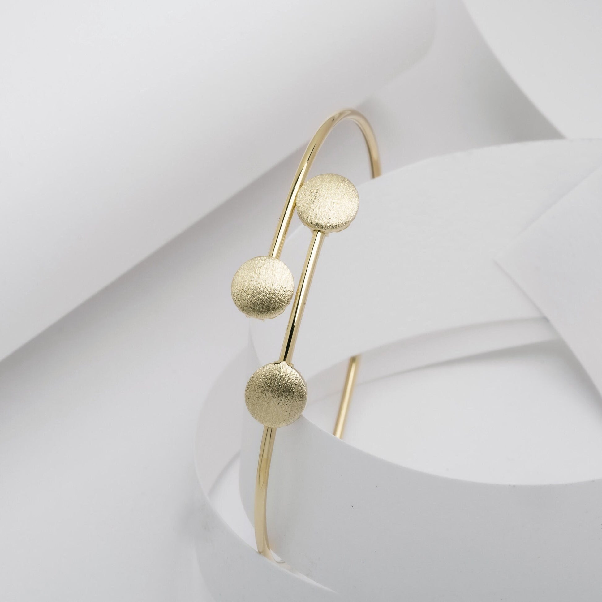 This photo features a minimalist gold open cuff bracelet with three textured round accents on the top.