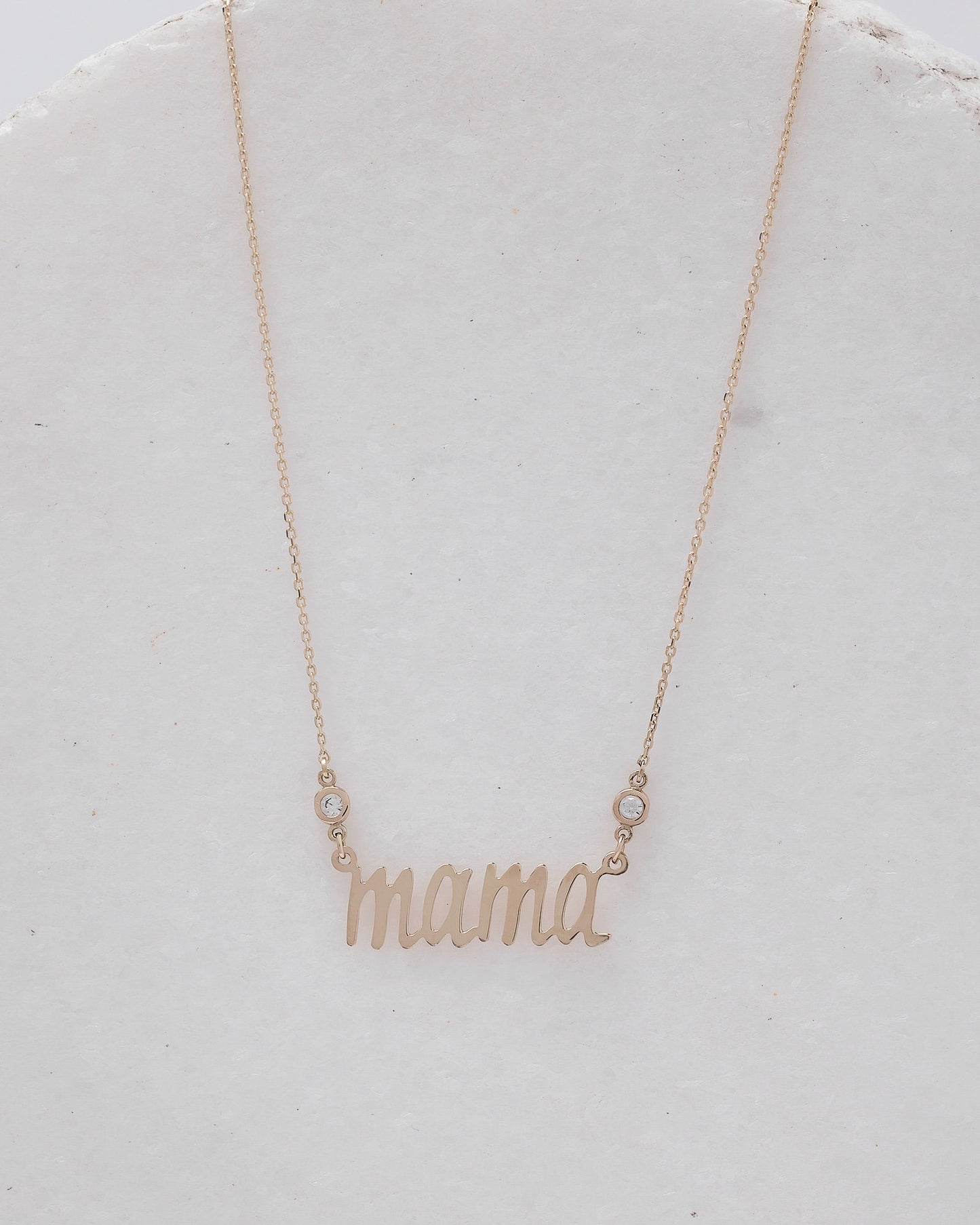 14k gold necklace with the word mama in a cursive script it is adorned with two cubic zirconia stones on each side of the word