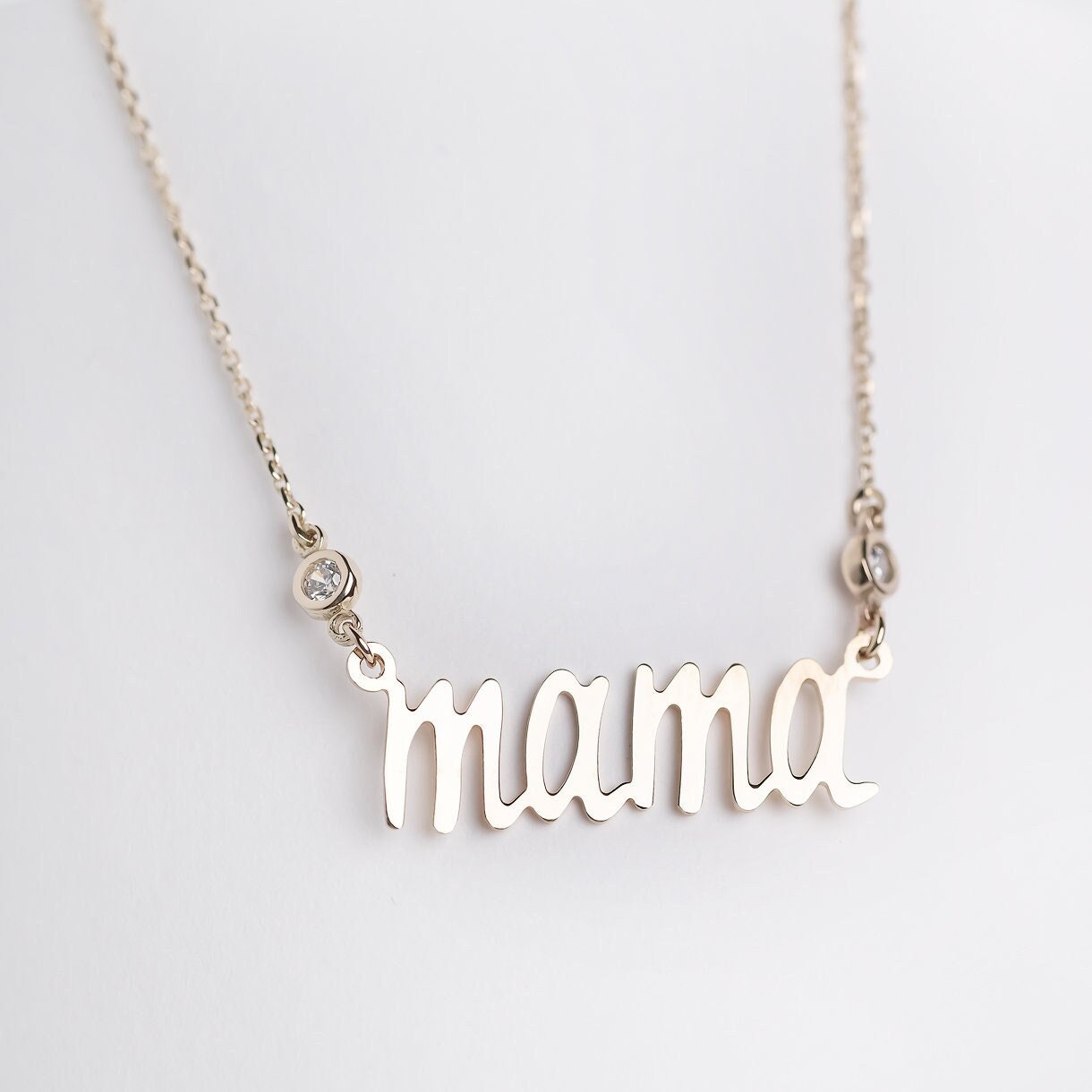 14k gold necklace with the word mama in a cursive script it is adorned with two cubic zirconia stones on each side of the word