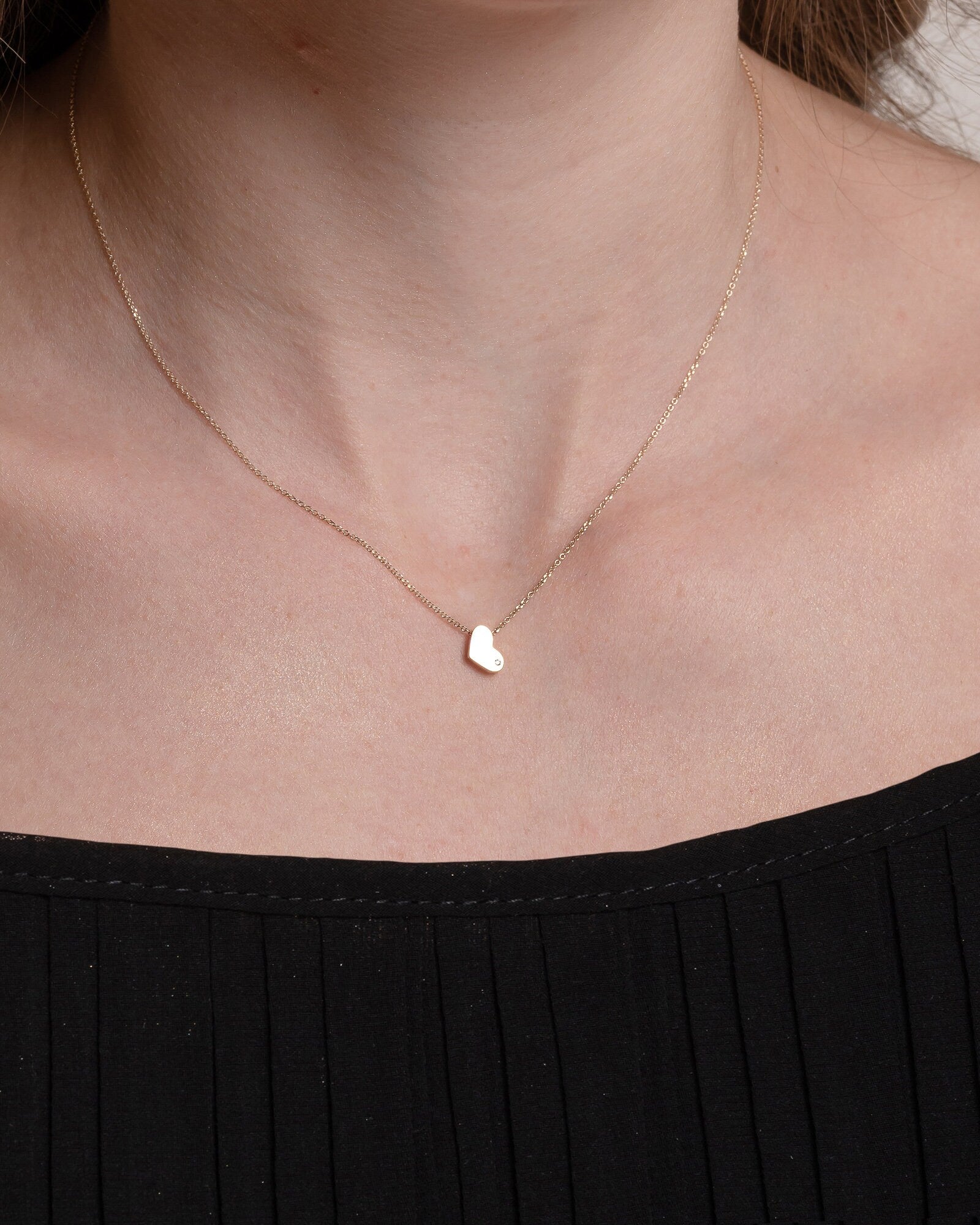 14k gold heart necklace with a modern, slightly asymmetrical design, with smooth, polished edges. A small diamond is embedded at the bottom right corner