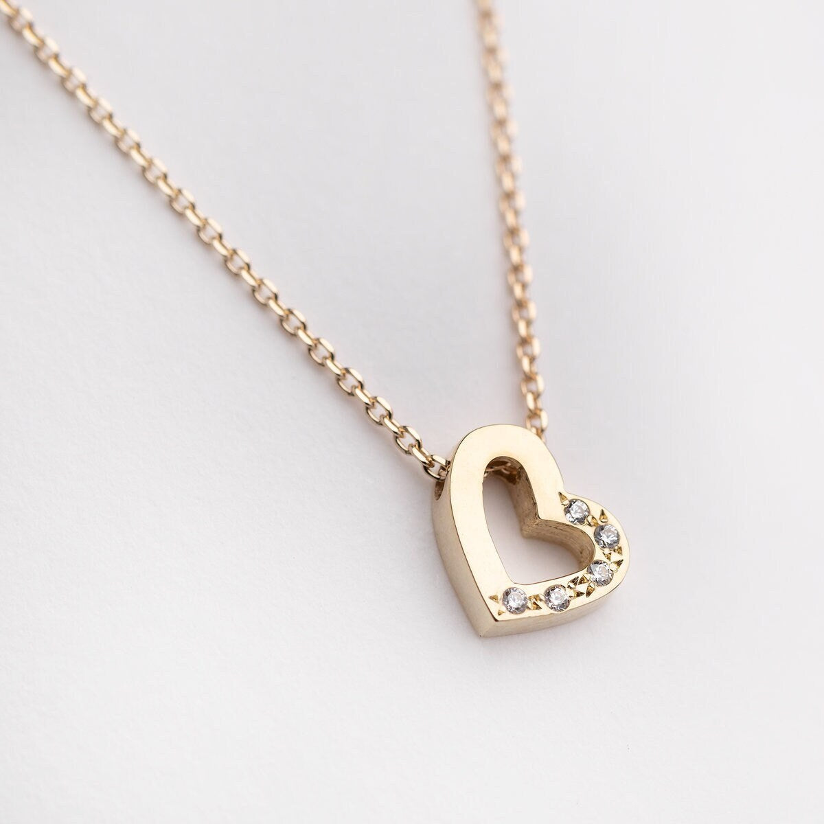 A delicate heart-shaped necklace crafted from 14k solid gold, featuring cubic zirconia stones adorning one half of the heart.