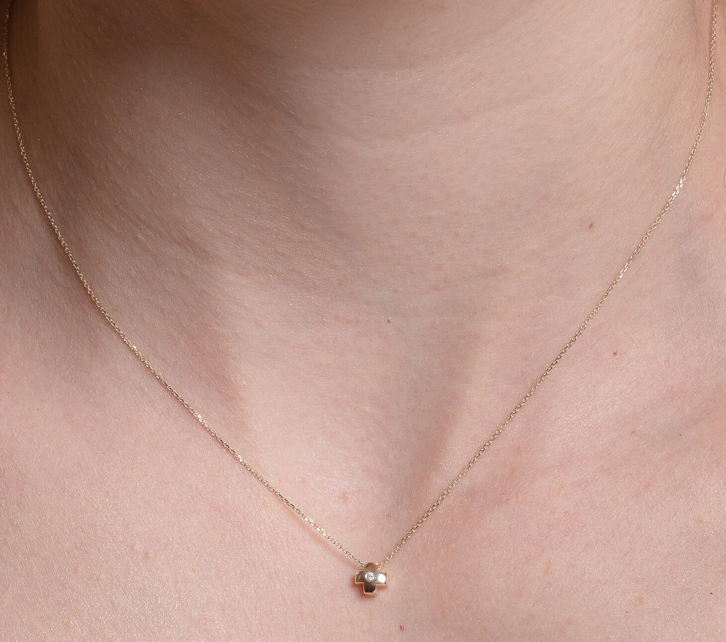 small diamond cross necklace in 14k gold for women worn by a model 