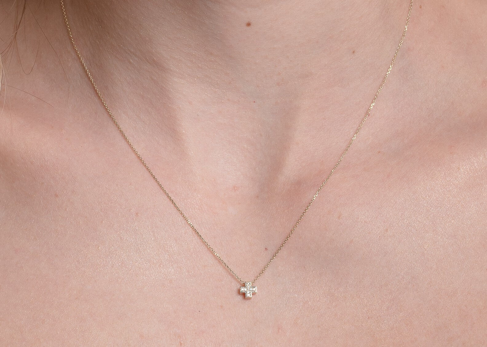 paved small cross necklace in 14k yellow gold for women worn by a model 