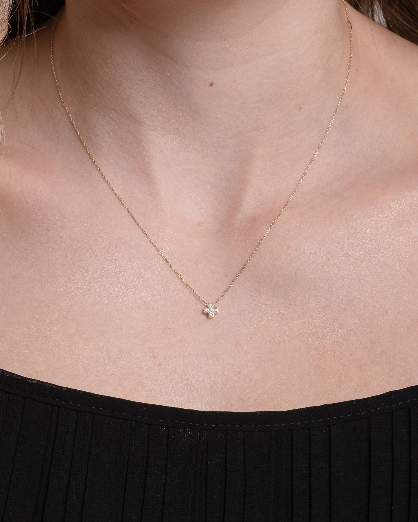 paved small cross necklace in 14k yellow gold for women worn by a model 