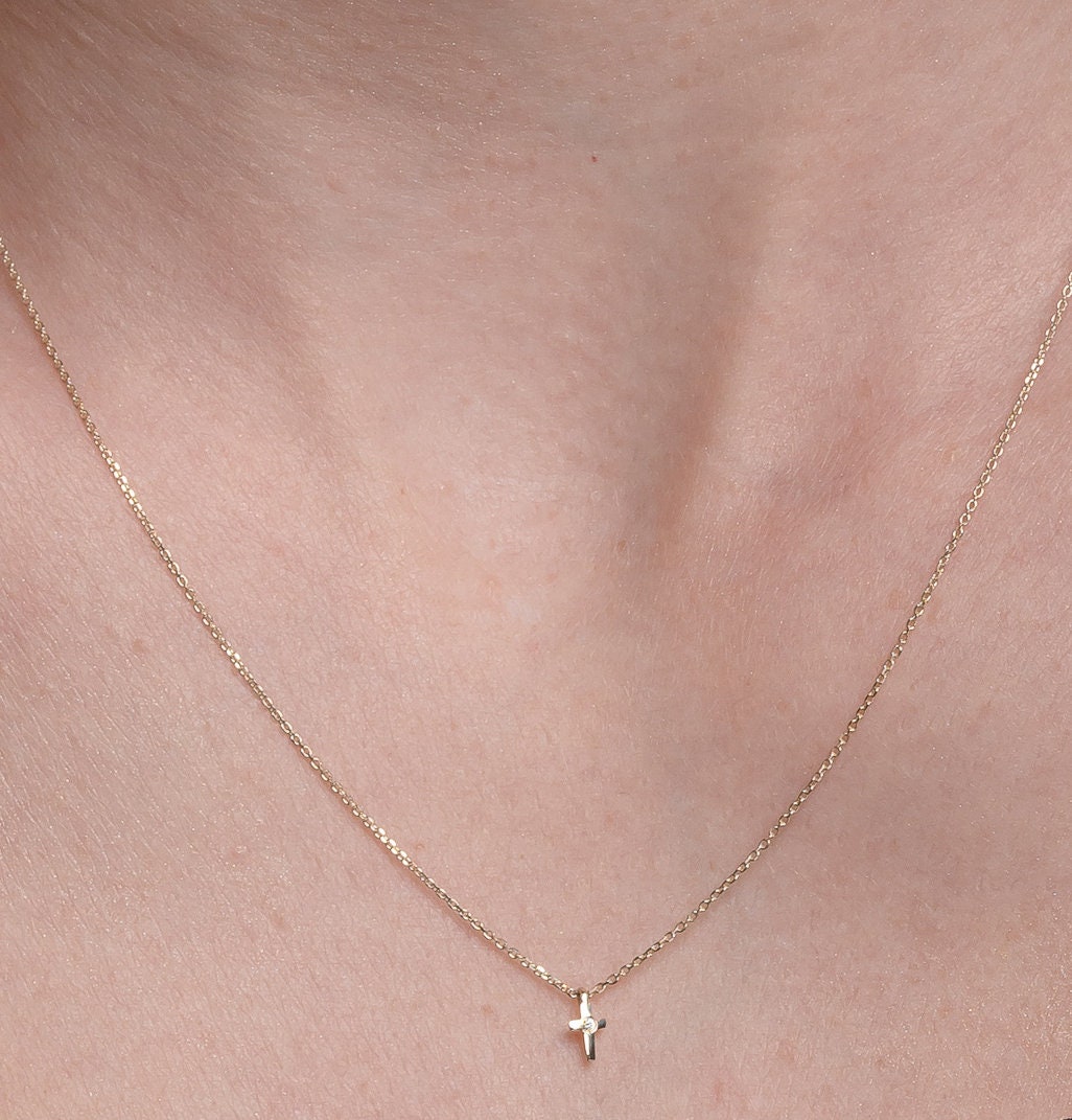 tiny diamond cross necklace in 14k yellow gold worn by a model 