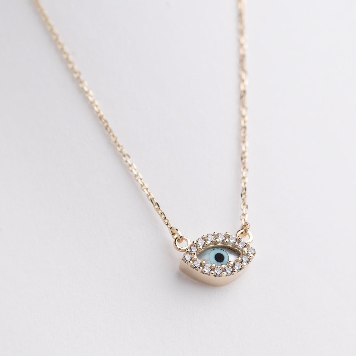 An oval-shaped evil eye necklace featuring mother of pearl and cubic zirconia stones, set in 14k gold for women.