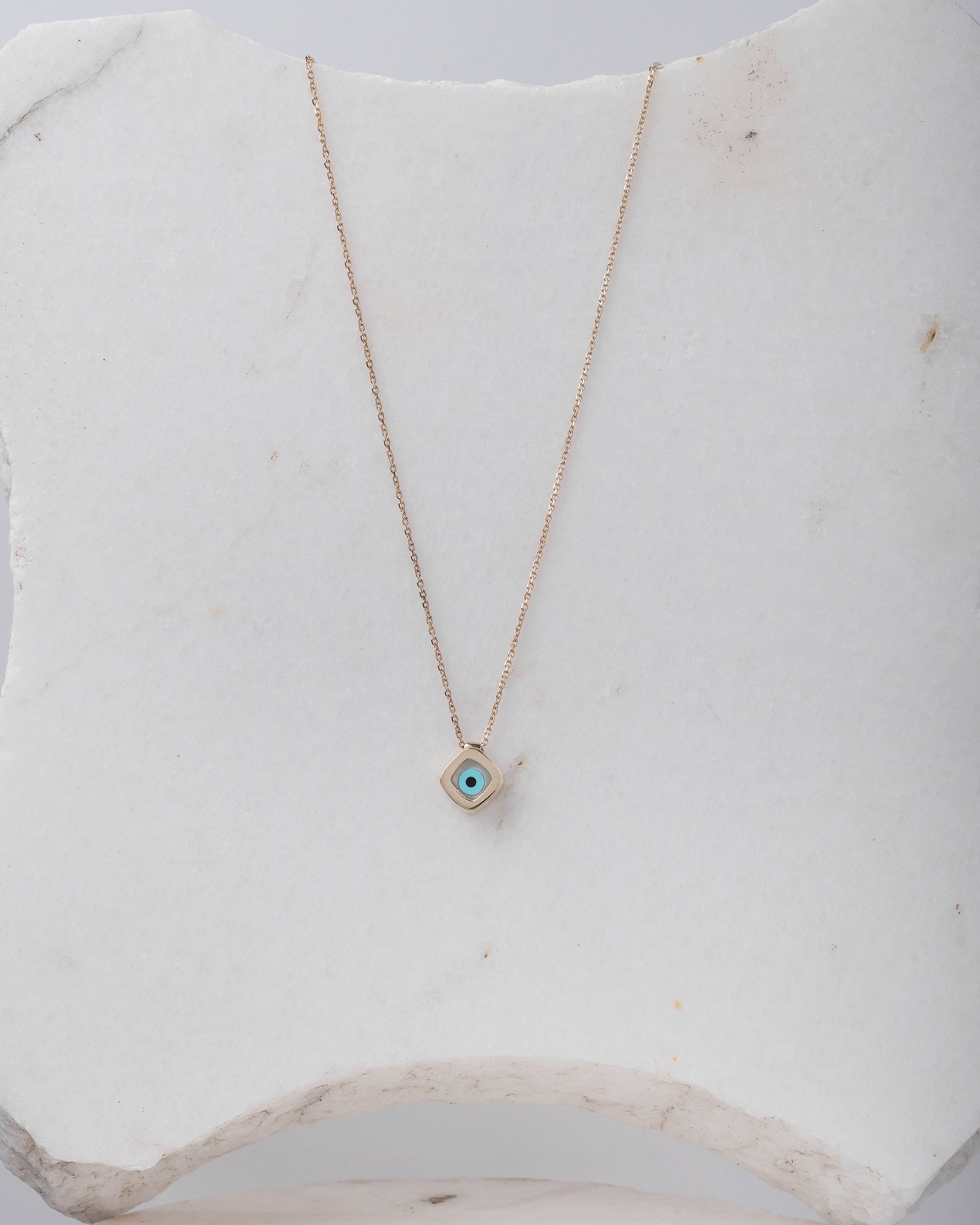 A mother-of-pearl evil eye necklace in 14k gold, fashioned in a rhombus shape.