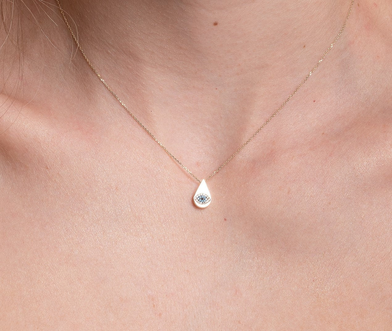 A drop-shaped evil eye necklace, encrusted with cubic zirconia stones and set in 14k gold worn by a model 