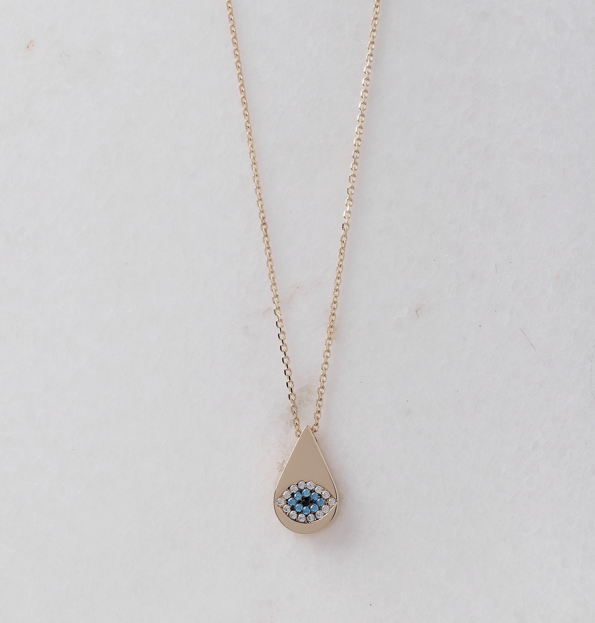 A drop-shaped evil eye necklace, encrusted with cubic zirconia stones and set in 14k gold.