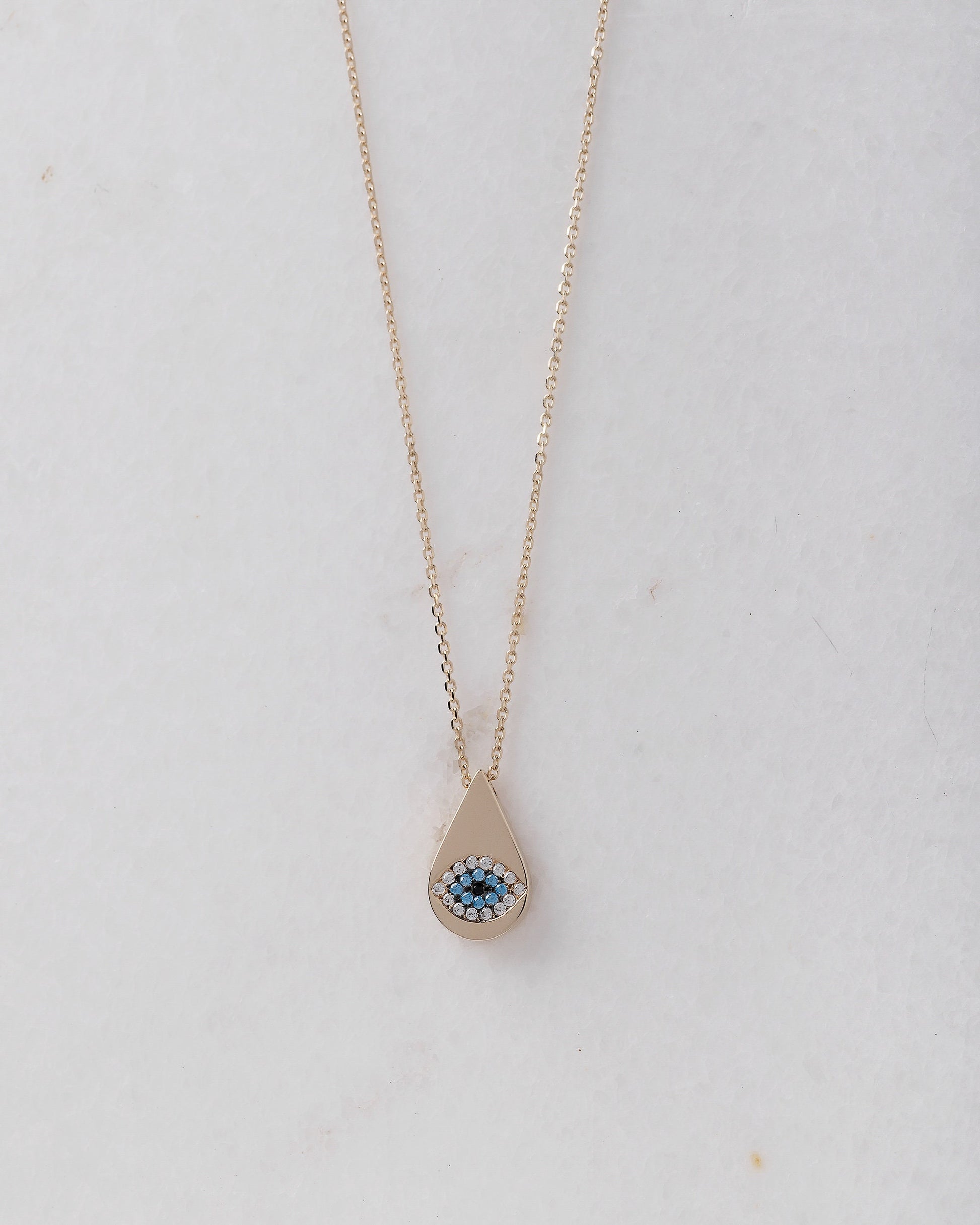 A drop-shaped evil eye necklace, encrusted with cubic zirconia stones and set in 14k gold.