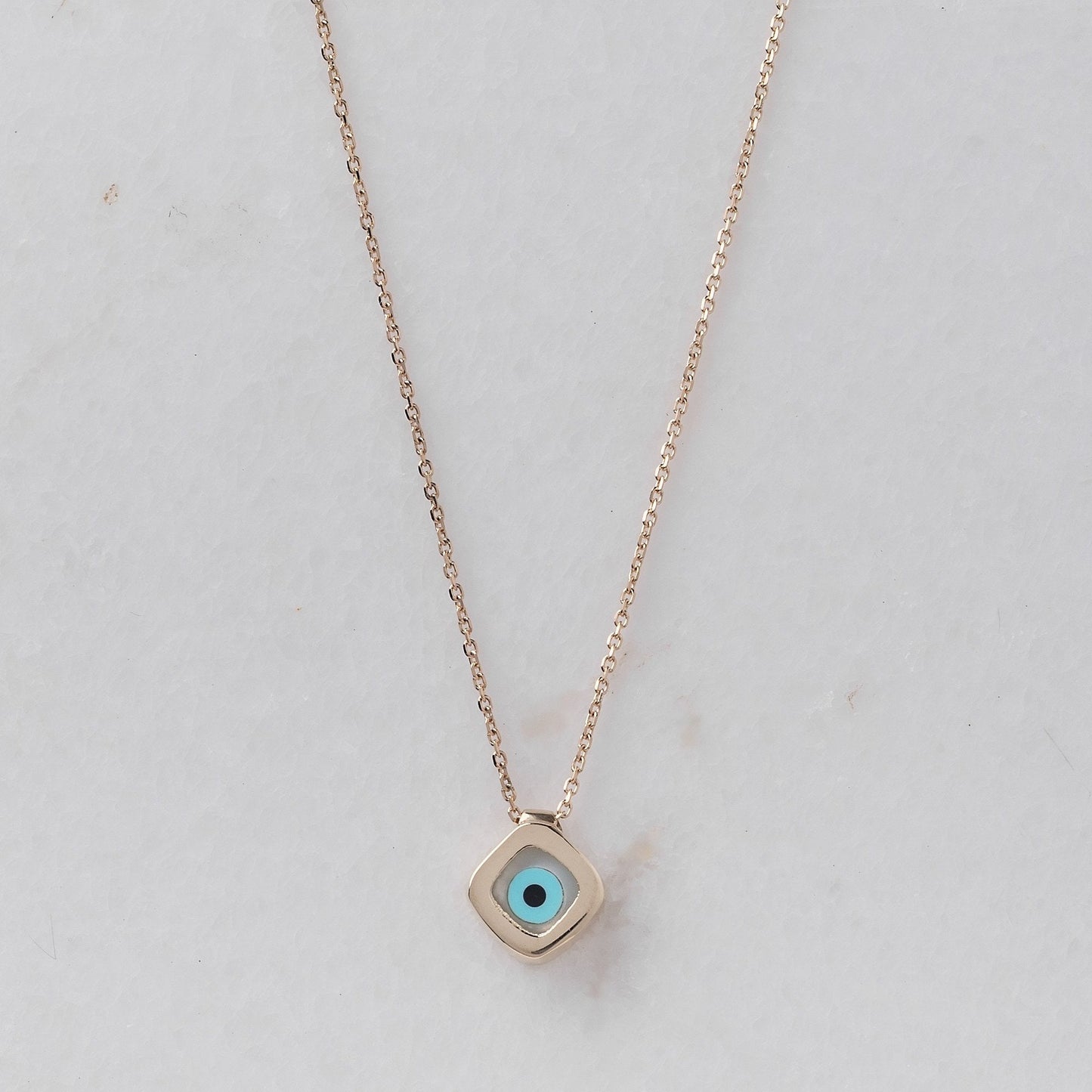 A mother-of-pearl evil eye necklace in 14k gold, fashioned in a rhombus shape.