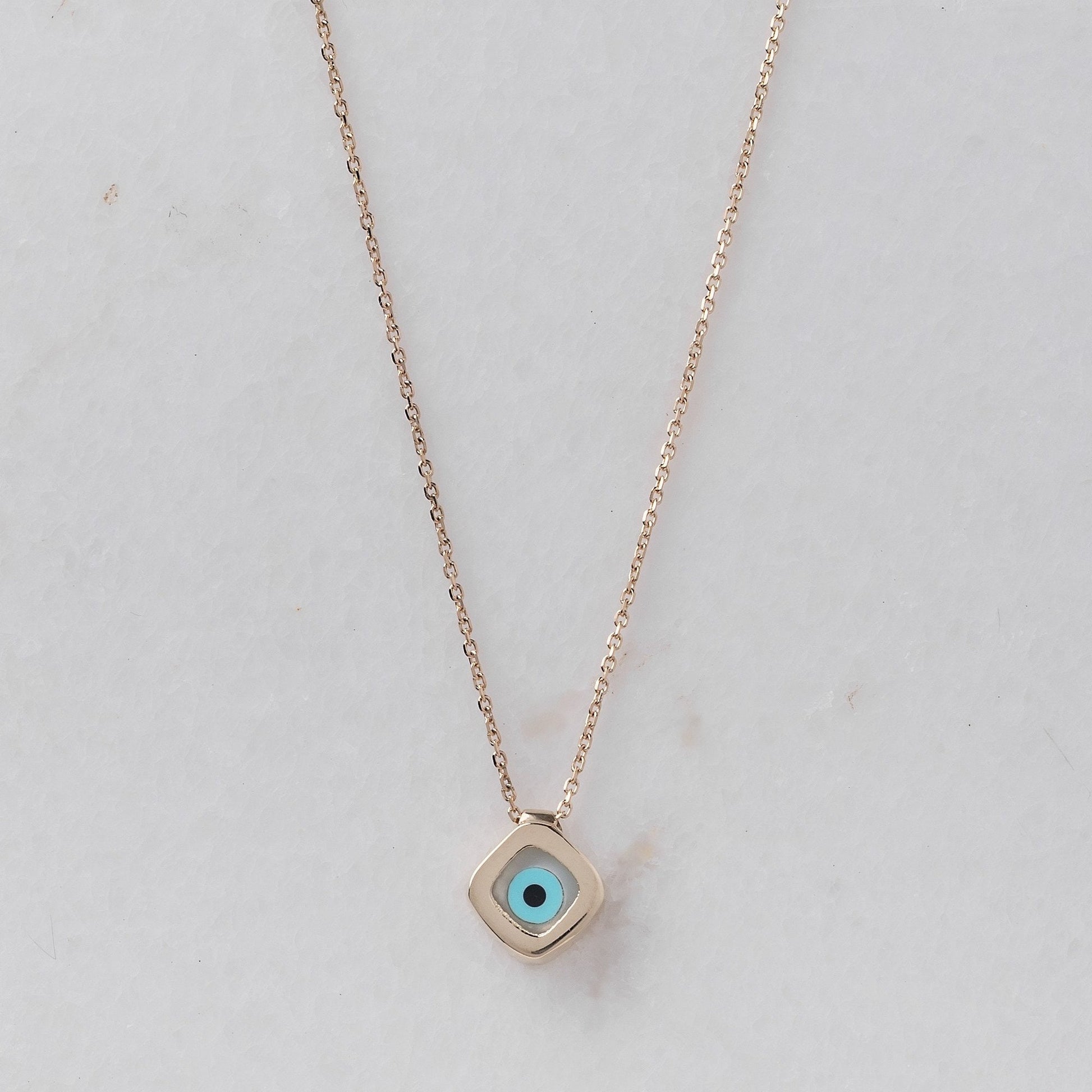 A mother-of-pearl evil eye necklace in 14k gold, fashioned in a rhombus shape.