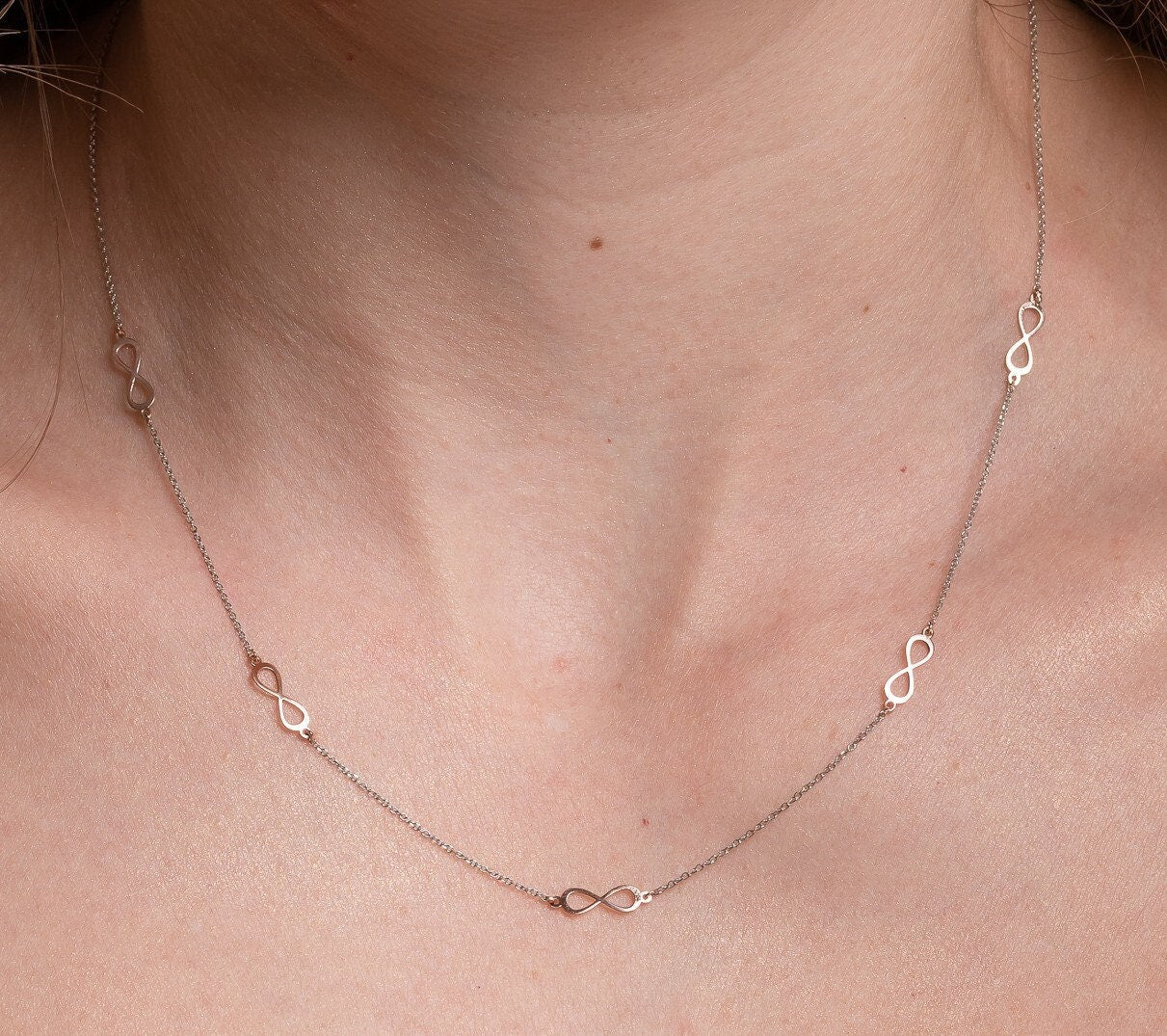 A station necklace featuring five infinity symbols in rose gold, complemented by a chain in white gold.