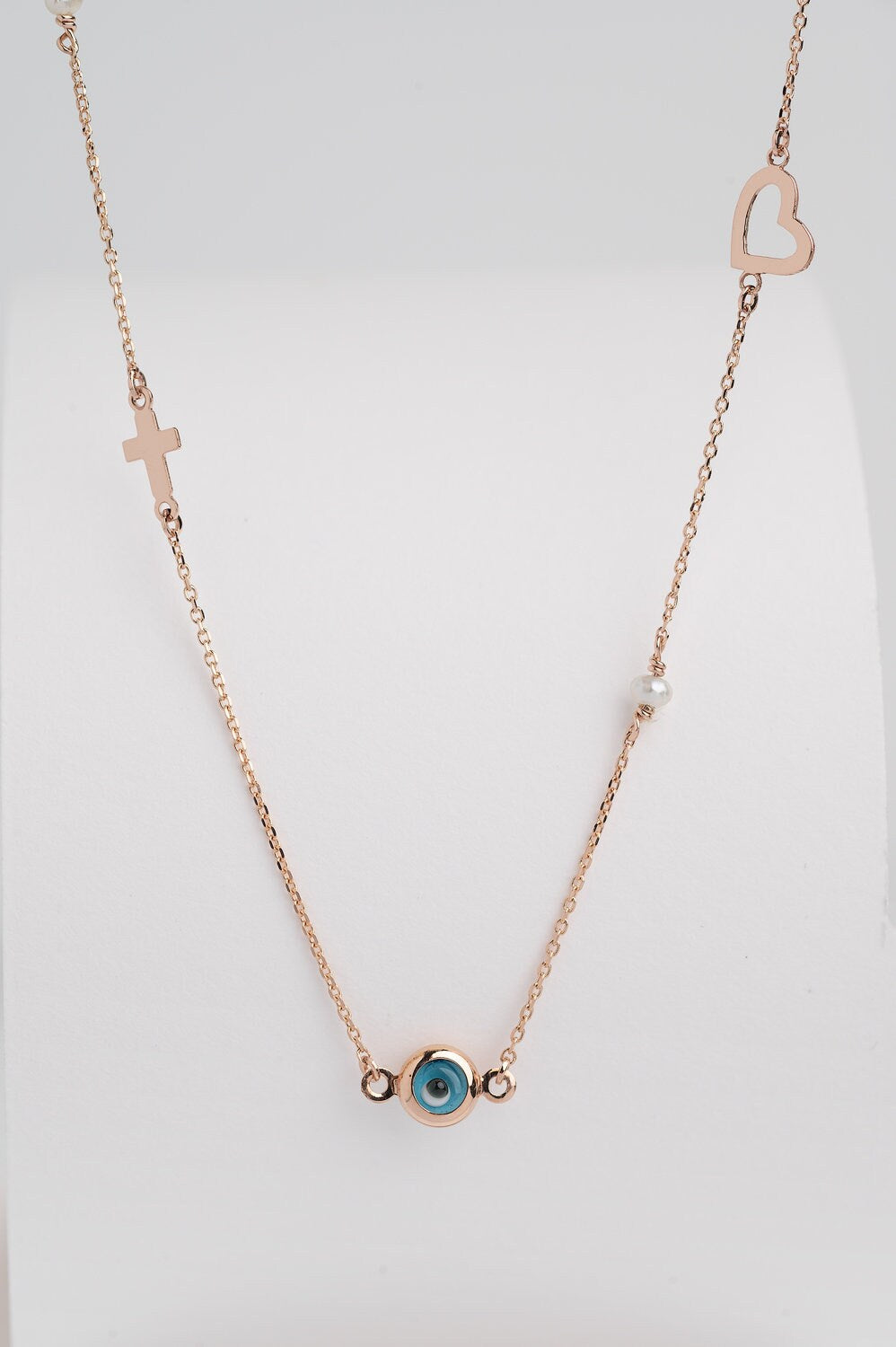 A station necklace featuring an evil eye, heart, cross, pearls, and a turquoise stone, all crafted in 14k gold.