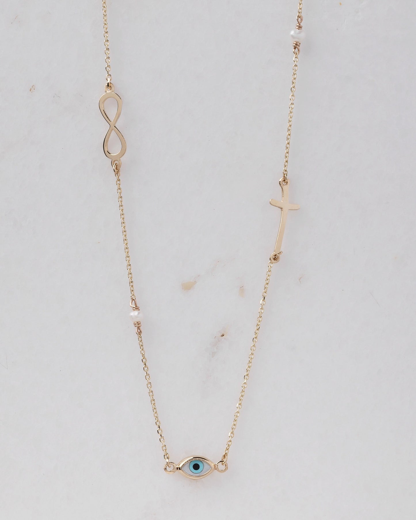 Station necklace featuring an evil eye, a cross, an infinity symbol, turquoise, and pearls in 14k gold.