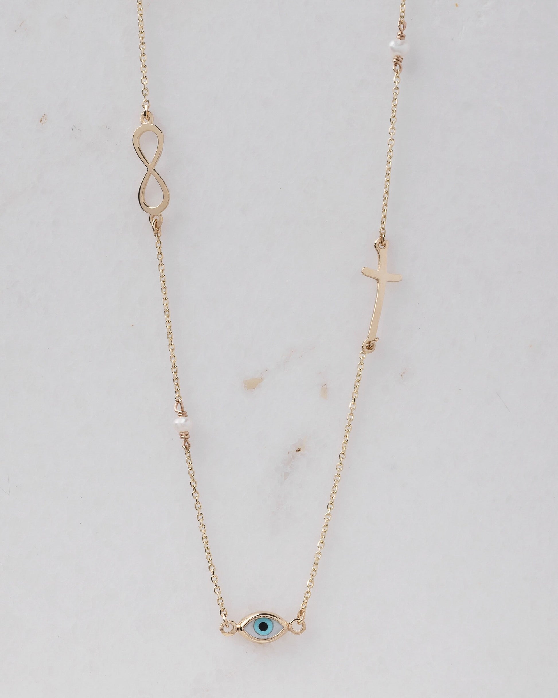 Station necklace featuring an evil eye, a cross, an infinity symbol, turquoise, and pearls in 14k gold.