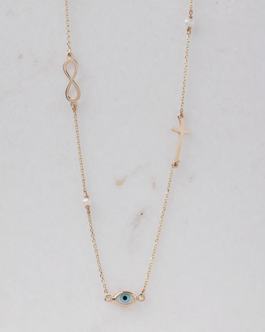 Station necklace featuring an evil eye, a cross, an infinity symbol, turquoise, and pearls in 14k gold.