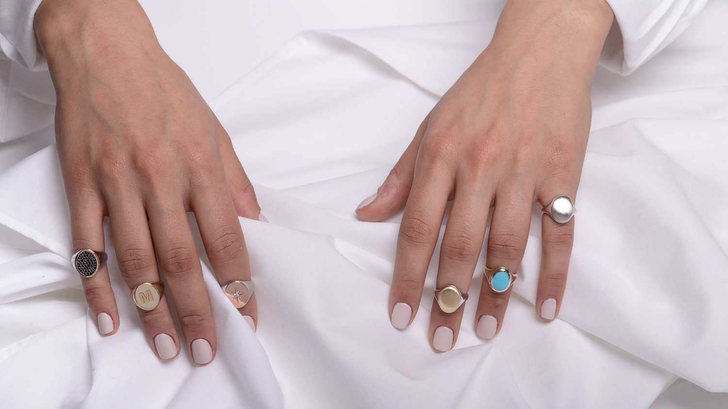 stylish collection of signet rings, featuring various designs worn by a model