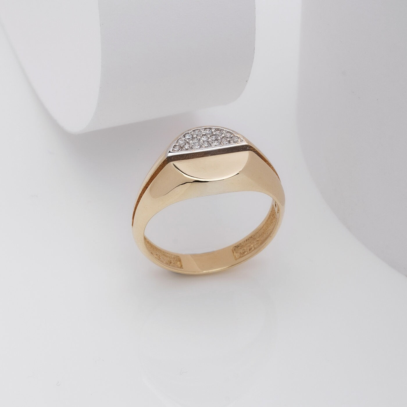 A round signet ring crafted in 14k gold, with half of the top part encrusted with white cubic zirconia stones.