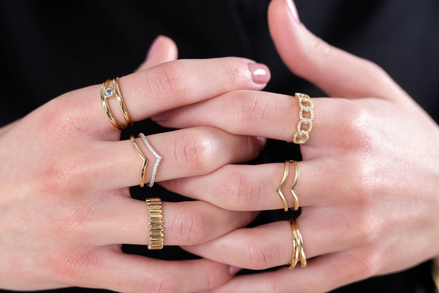 This image features hands adorned with delicate gold rings, showcasing a variety of styles including gemstone accents, twisted bands, and minimalist designs.