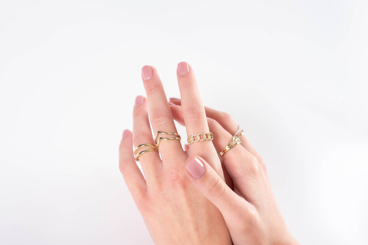 The image showcases a hand adorned with multiple gold rings and bracelets. One ring features a chain-link design with diamonds, while another has a sleek chevron style.