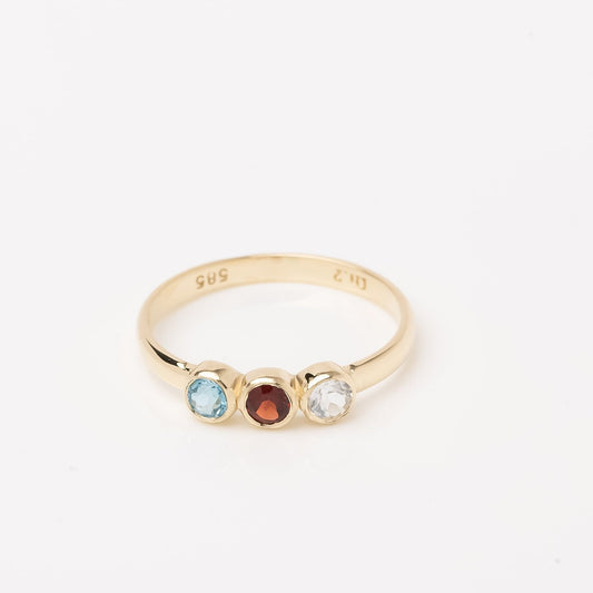 A handmade ring featuring three birthstones set in a bezel, crafted in 14k solid gold.