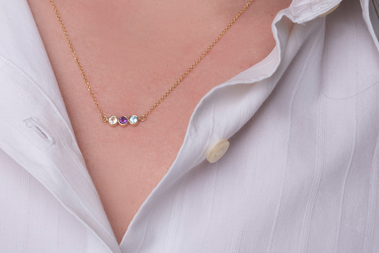 A 14k gold birthstone necklace for women, featuring three stones in a bezel setting.