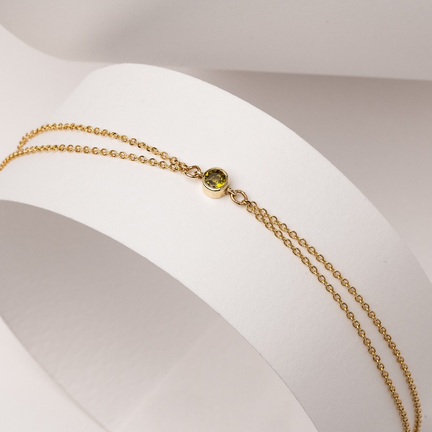 A handmade bracelet featuring a single birthstone in a bezel setting, crafted in 14k gold with a double chain design.