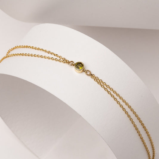 A handmade bracelet featuring a single birthstone in a bezel setting, crafted in 14k gold with a double chain design.