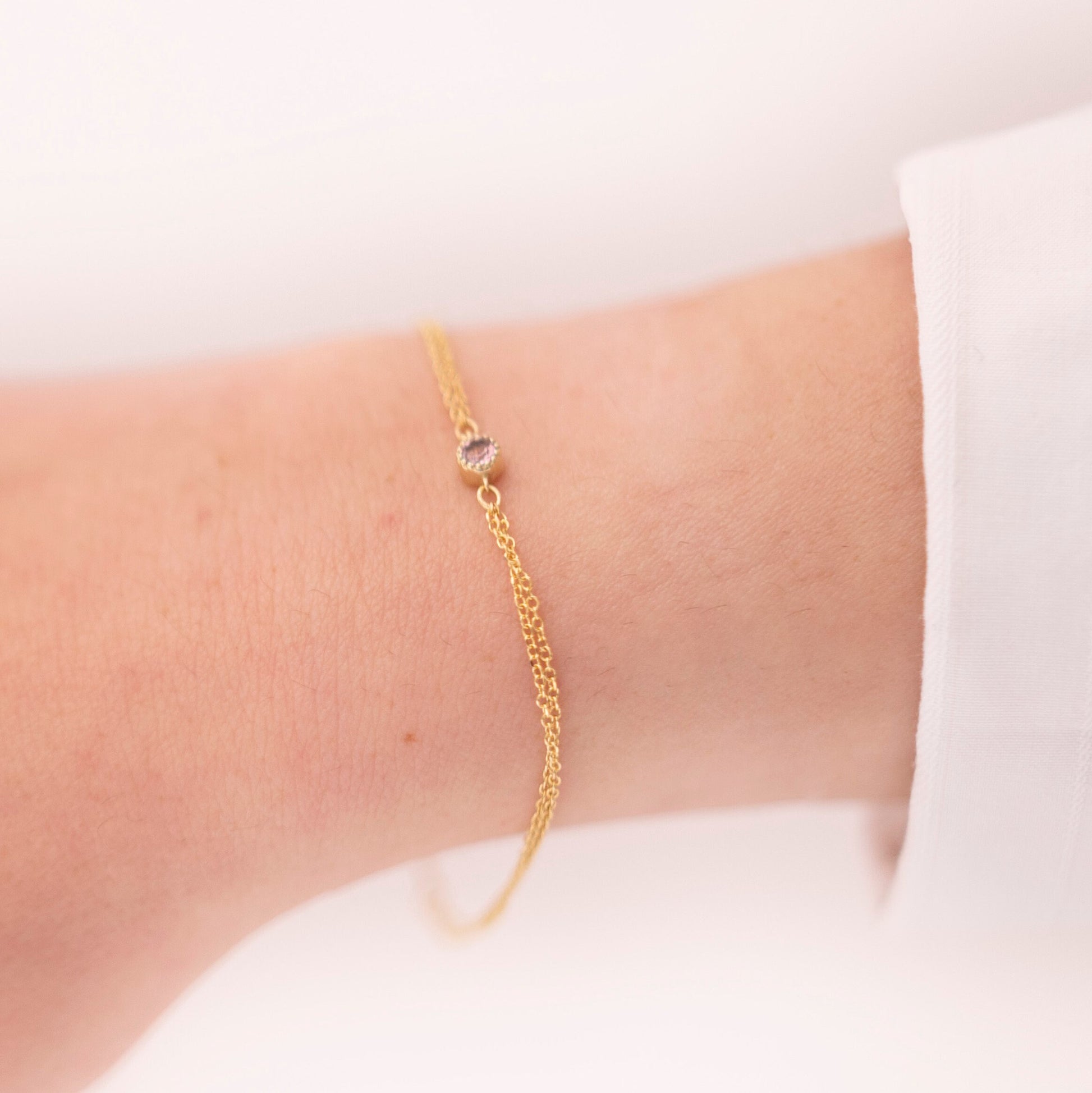 A handmade bracelet featuring a single birthstone set in 14k gold, complemented by a double chain design.