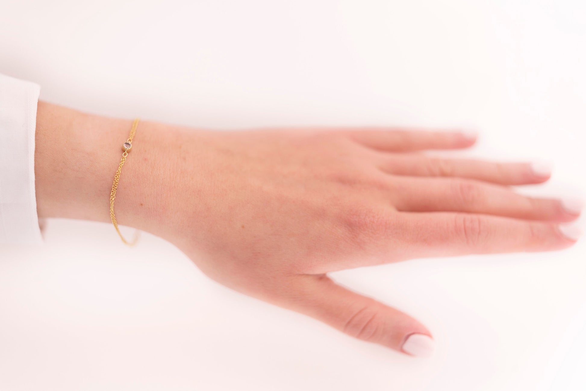 A handmade bracelet featuring a single birthstone set in 14k gold, complemented by a double chain design.