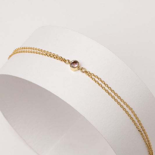 A handmade bracelet featuring a single birthstone set in 14k gold, complemented by a double chain design.