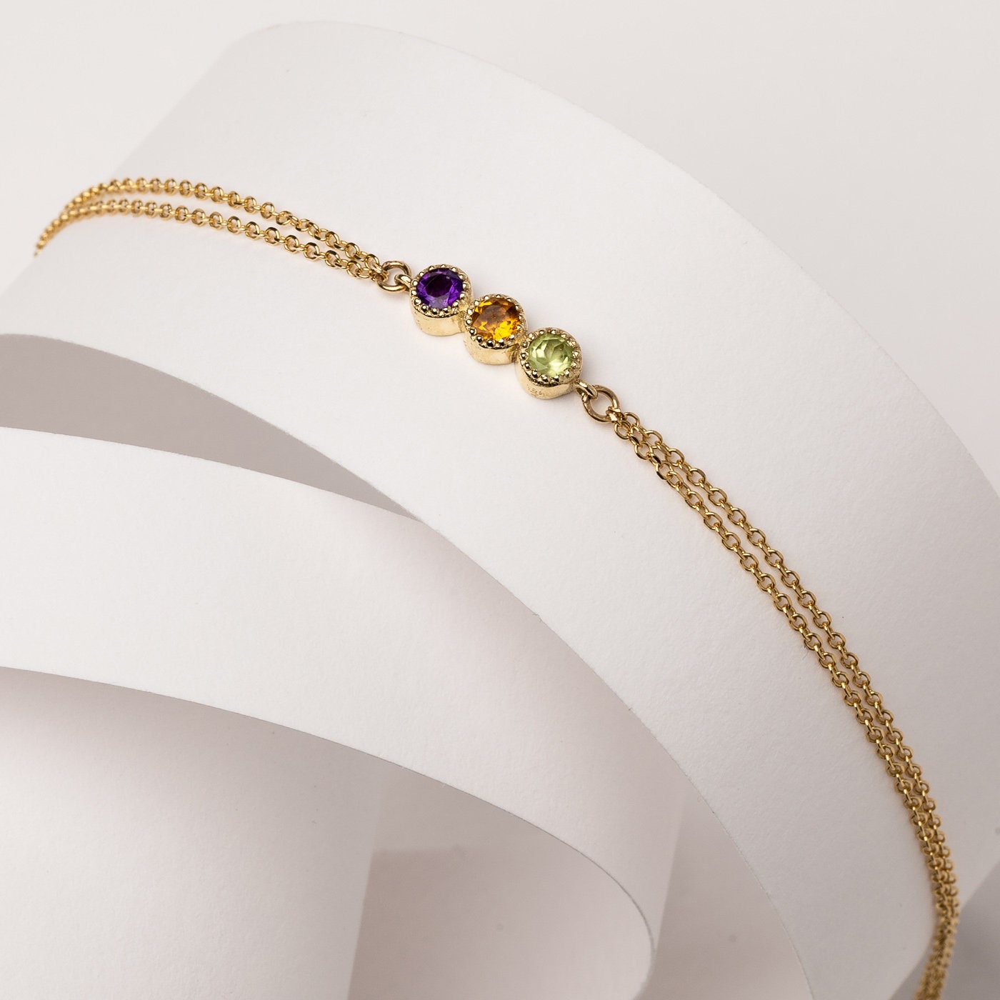 A handmade bracelet featuring three birthstones in a prong setting, crafted in 14k gold with a double chain design.