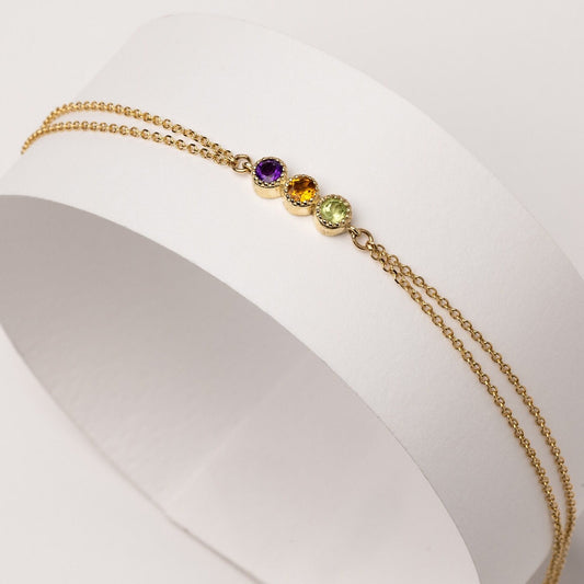 A handmade bracelet featuring three birthstones in a prong setting, crafted in 14k gold with a double chain design.