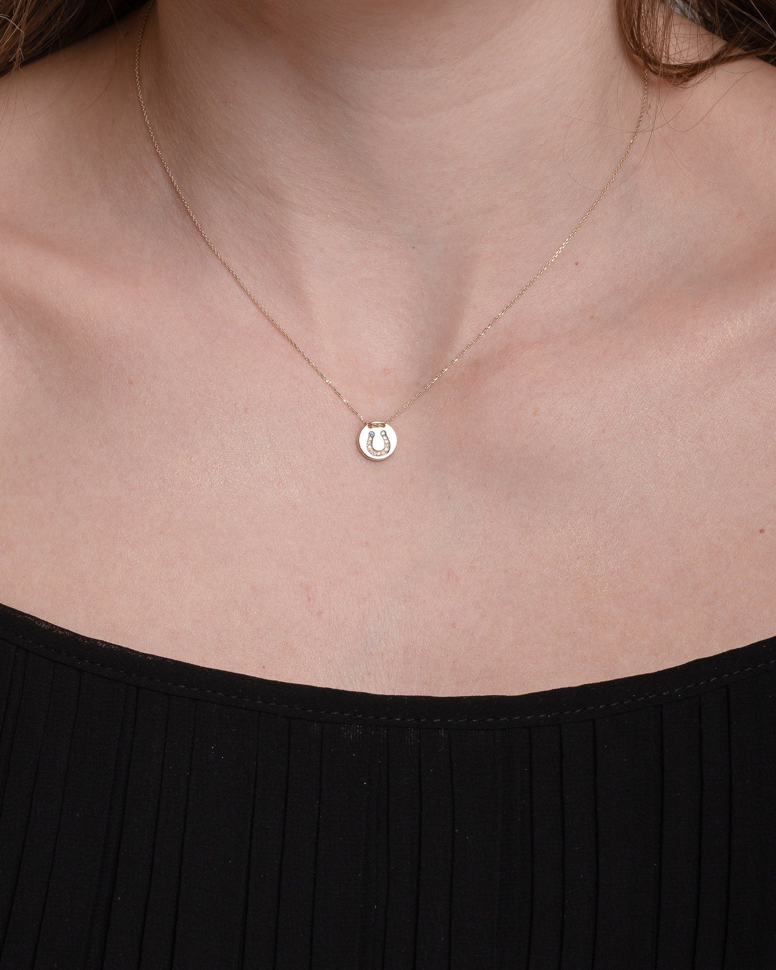 coin necklace in 14k gold with paved horseshoe worn by a model 