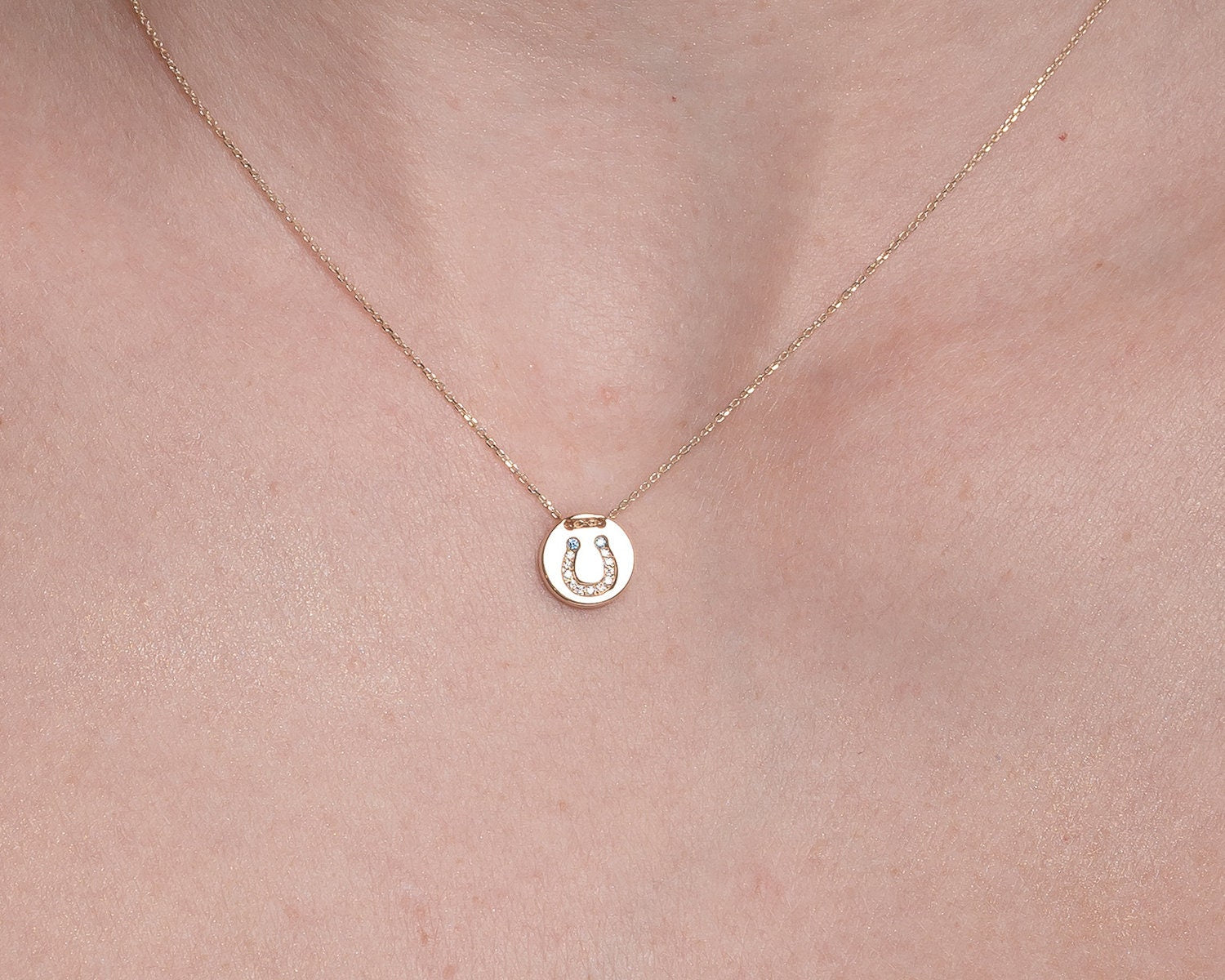 coin necklace in 14k gold with paved horseshoe worn by a model 