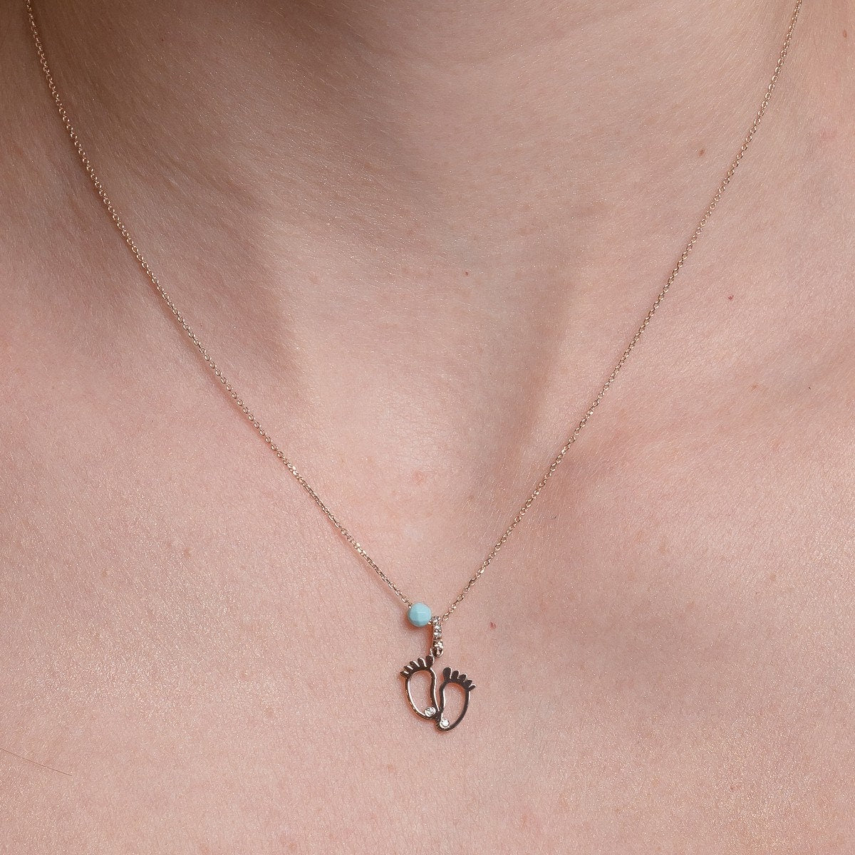 baby footprint necklace in 14k gold with cubic zirconia and turquoise stone worn by a model 