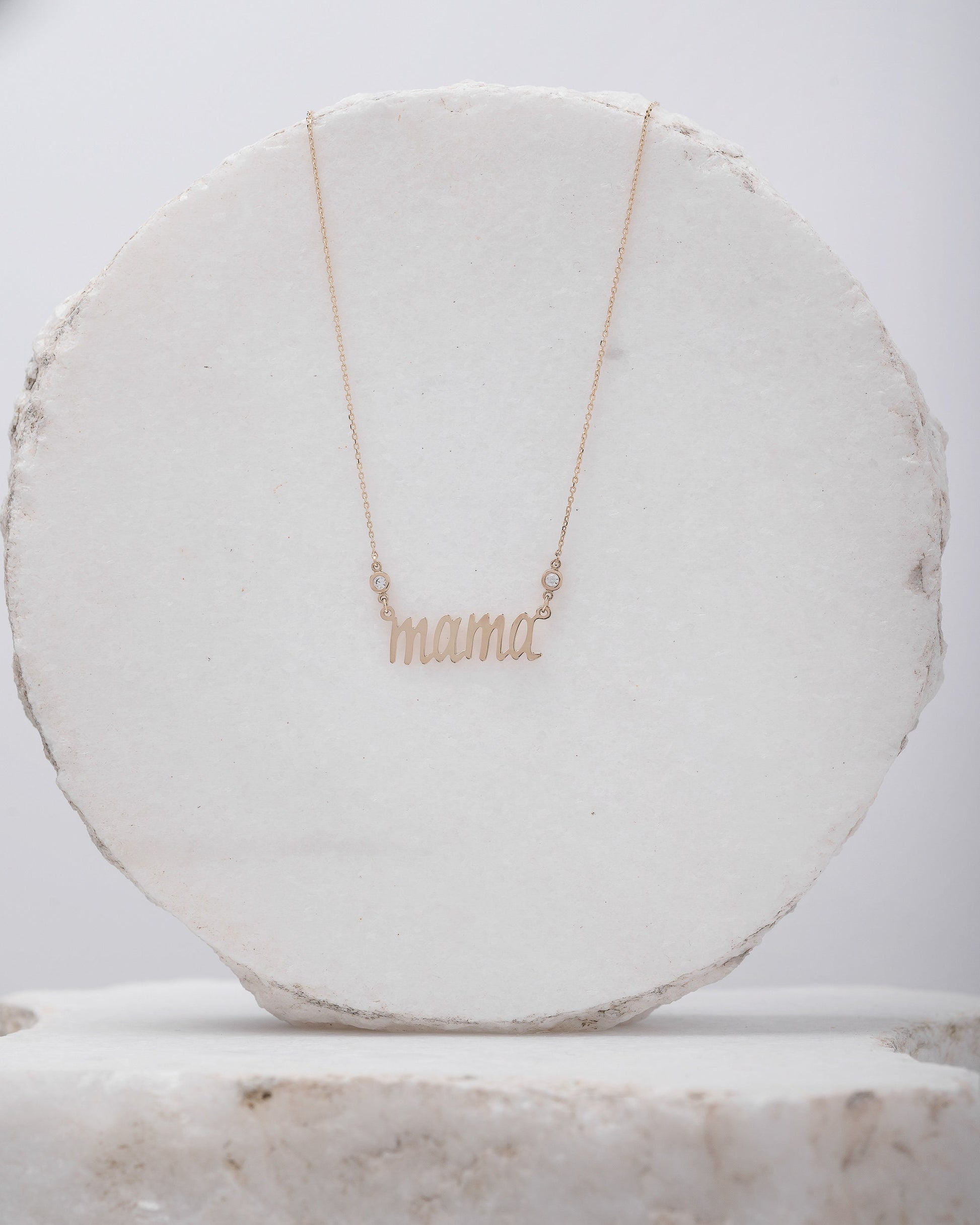 14k gold necklace with the word mama in a cursive script it is adorned with two cubic zirconia stones on each side of the word