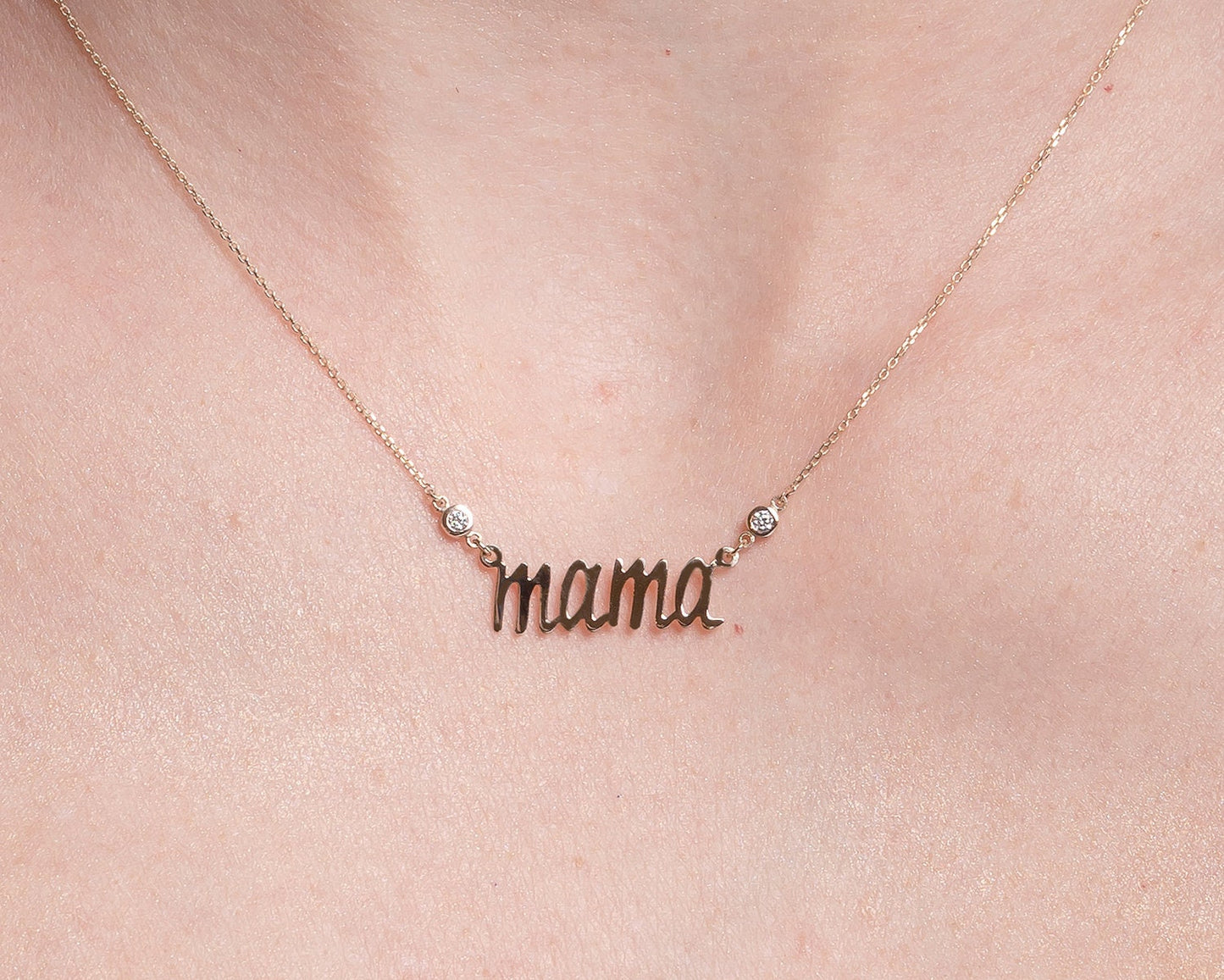 14k gold necklace with the word mama in a cursive script it is adorned with two cubic zirconia stones on each side of the word