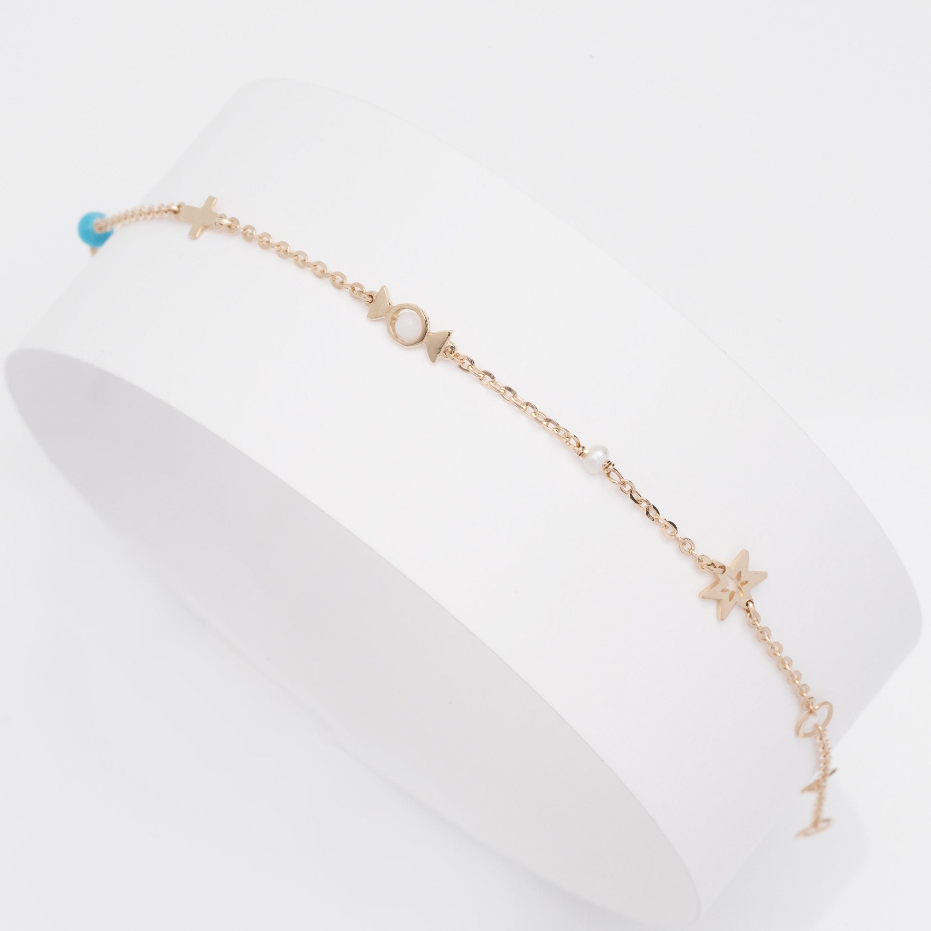 a hand wearing a 14k gold charm bracelet with star, candy, cross, pealr, turquoise