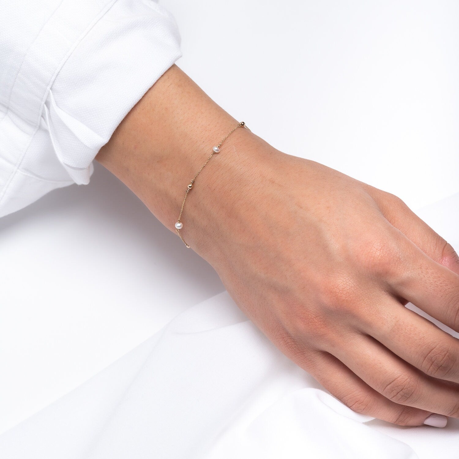 A model wears a Pearl Station Bracelet crafted from 14k solid gold, designed for women.