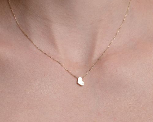 14k gold heart necklace with a modern, slightly asymmetrical design, with smooth, polished edges. A small diamond is embedded at the bottom right corner