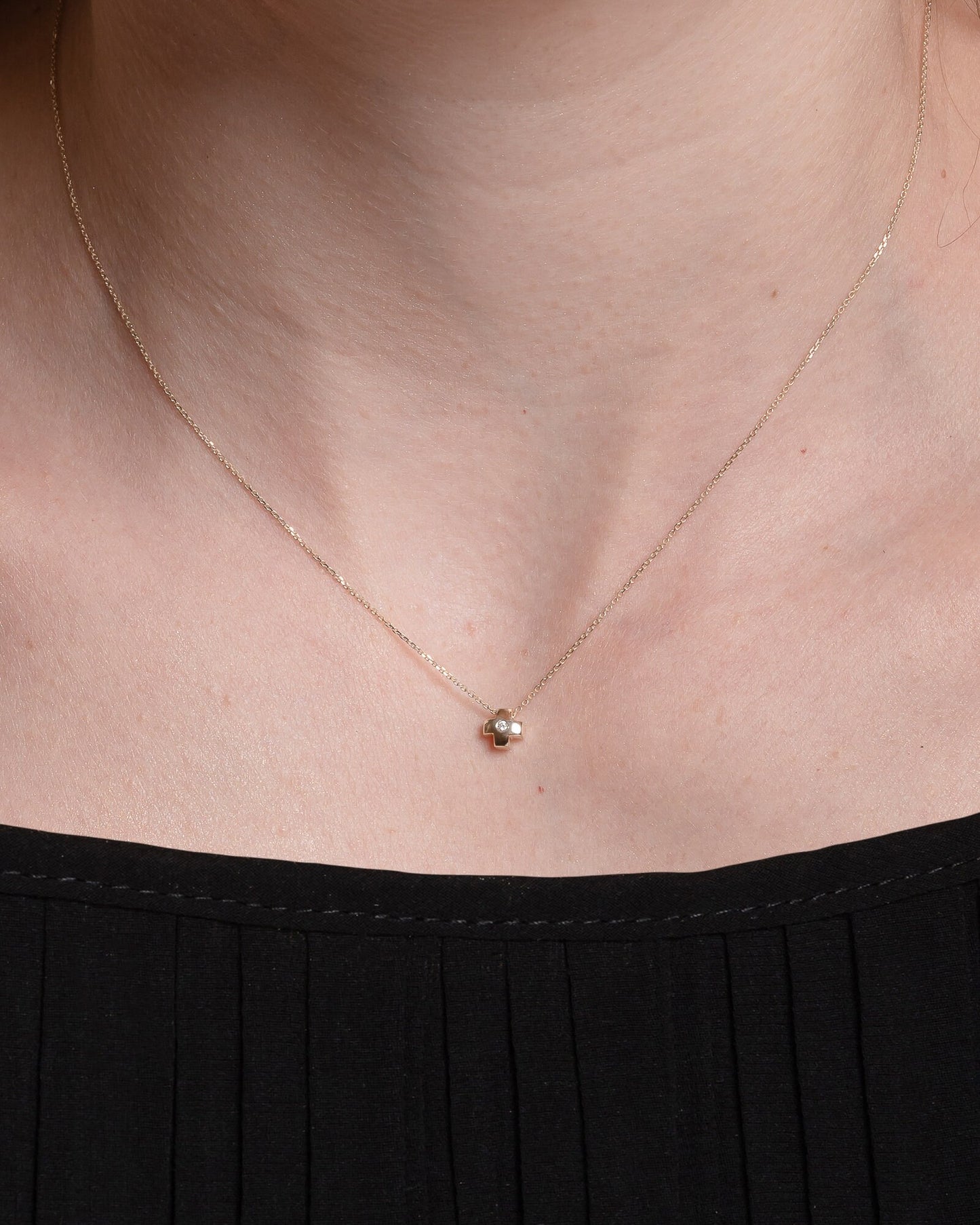 small diamond cross necklace in 14k gold for women worn by a model 